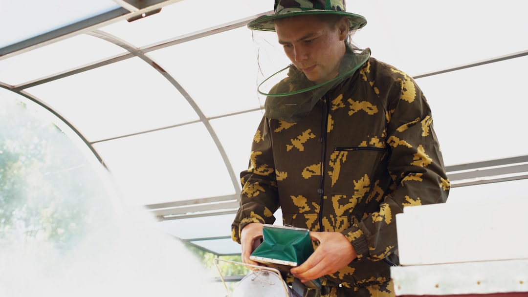 Young beekeeper smoking bees away from a beehive in an apiary on a sunny day