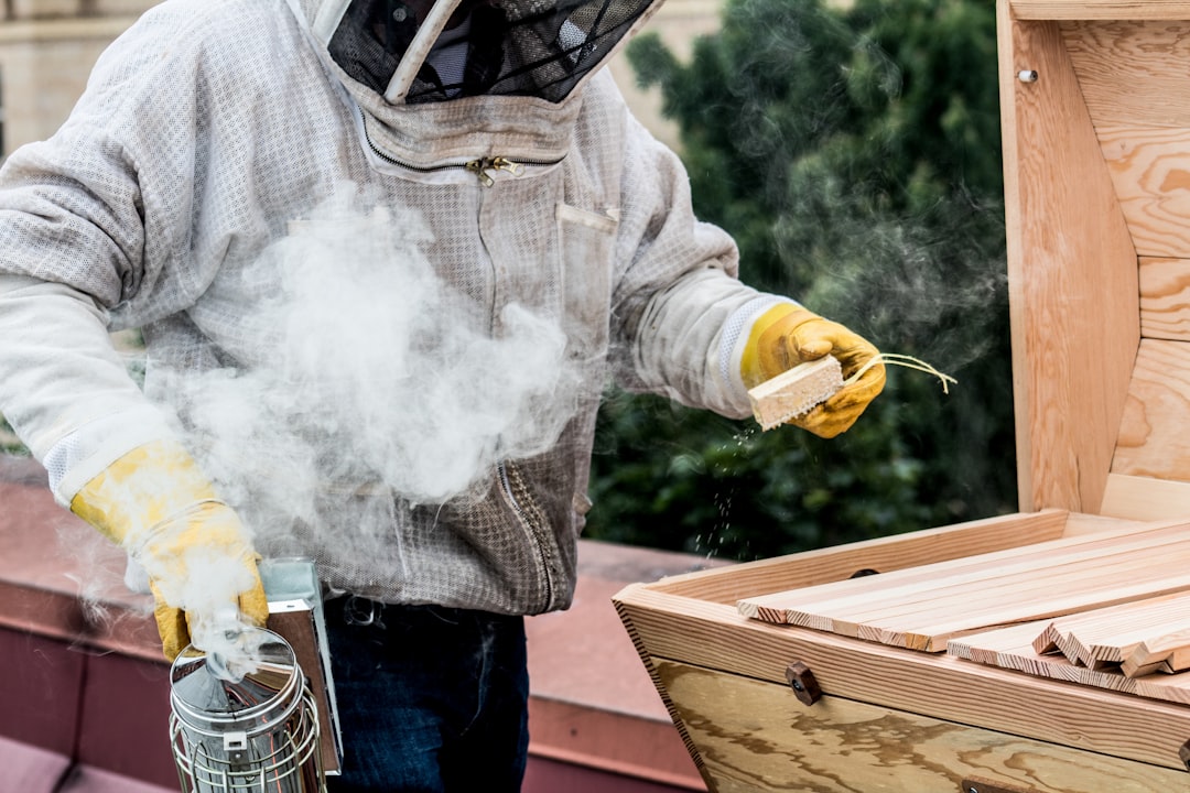 Person in long sleeve shirt holding yellow and silver hand tool, preparing beekeeping equipment